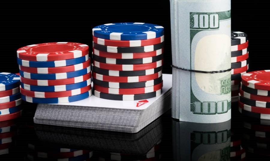 Poker chips stand on a deck of cards next to a stack of banknotes