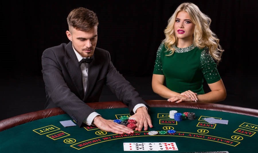 Couple playing poker at the green table. The blonde girl and a guy in a suit.